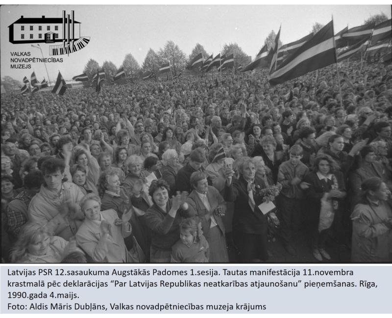 Augstākās padomes deputāti pēc deklarācijas pieņemšanas. Tautas manifestācija 11.novembra krastmalā. Cilvēku pūlis stāv ar karogiem un applaudē.