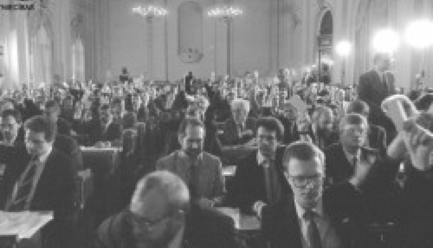melnbalta fotogrāfija ar cilvēku pilnu zāli, kurā delegāti paceļ balsošanas kartītes Latvijas neatkarības atjaunošanas procesa laikā.