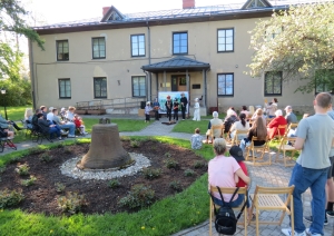 Muzeja galvenās ēkas lieveņa priekšā notiek bērnu teātra izrāde "Brēmenes muzikanti" zālienā un uz celiņiem skatītāji, bērnu vecāki, ģimenes sež un skatās izrādes norisi. 